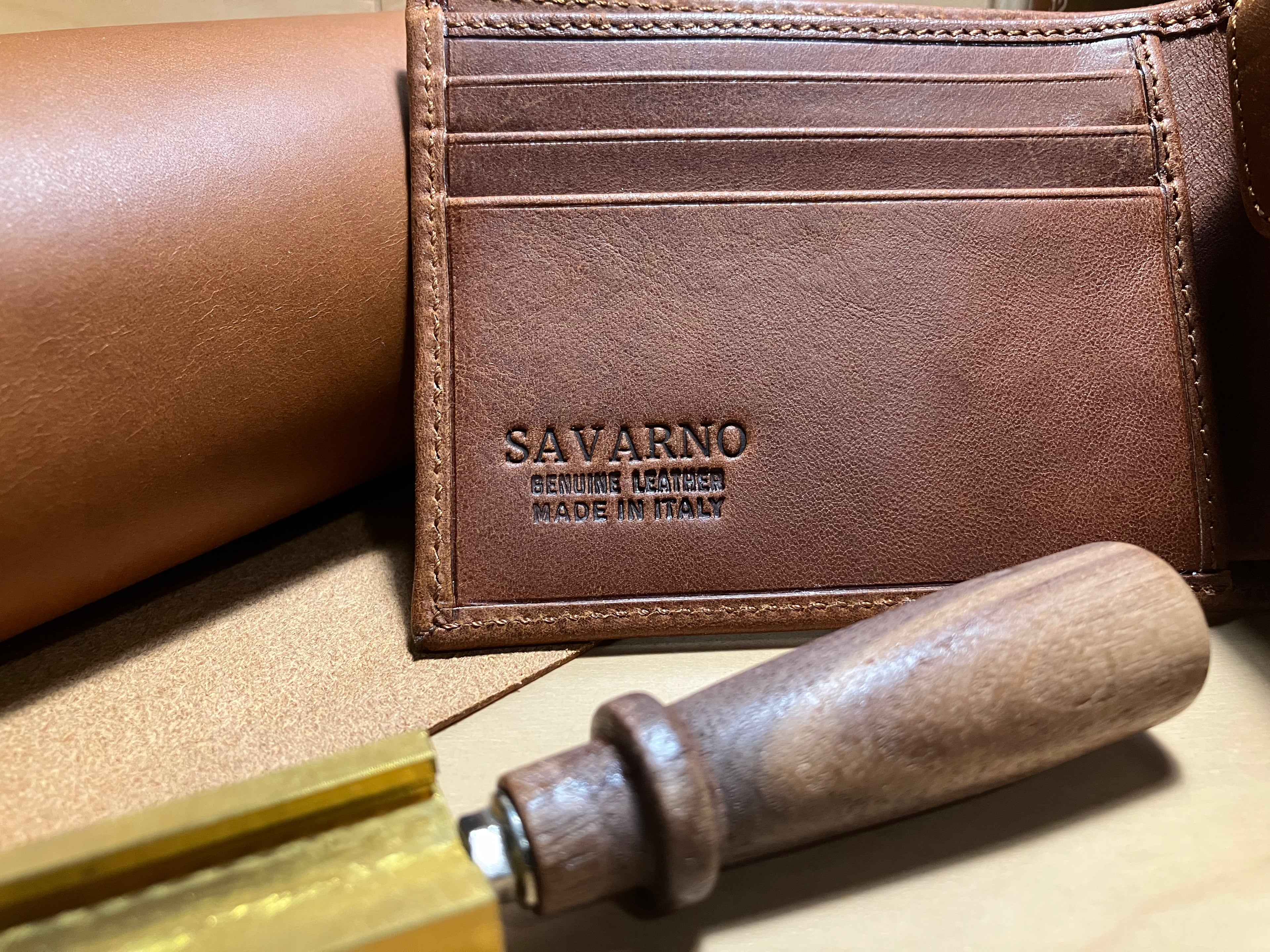 Savarno brown leather bi-fold wallet on a backdrop made of leather hide, and an embossing tool