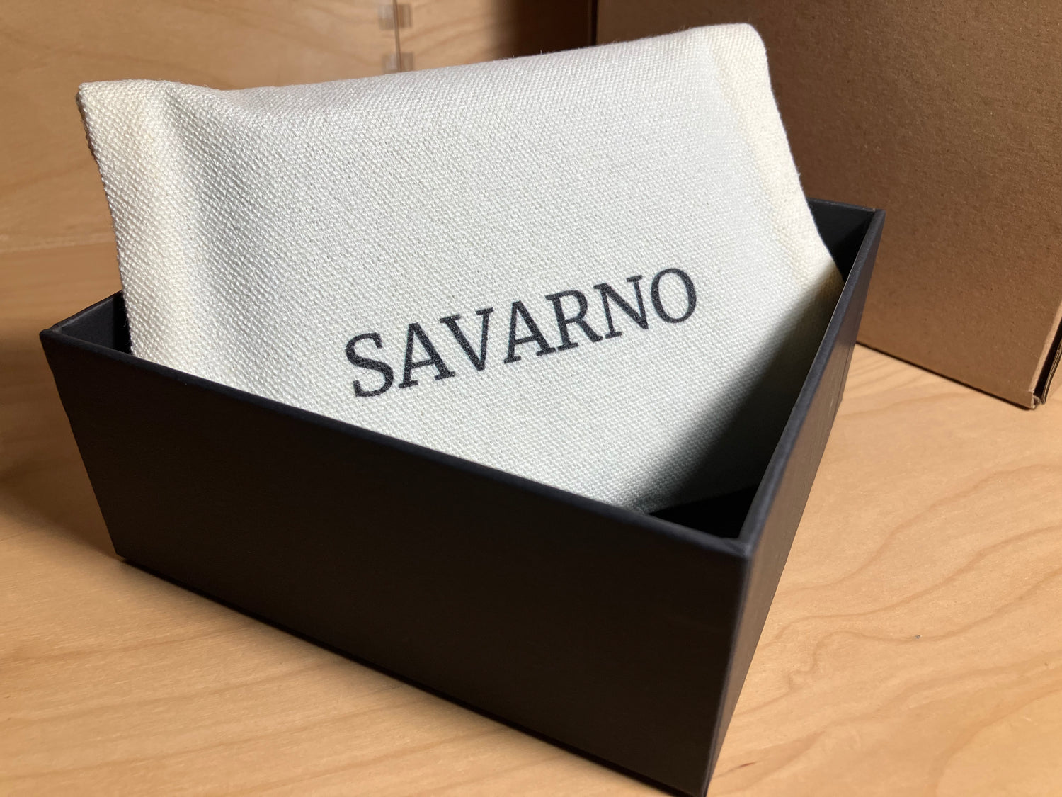 Savarno wallet in its premium gift box and soft dust bag, with cardboard shipping box in the background